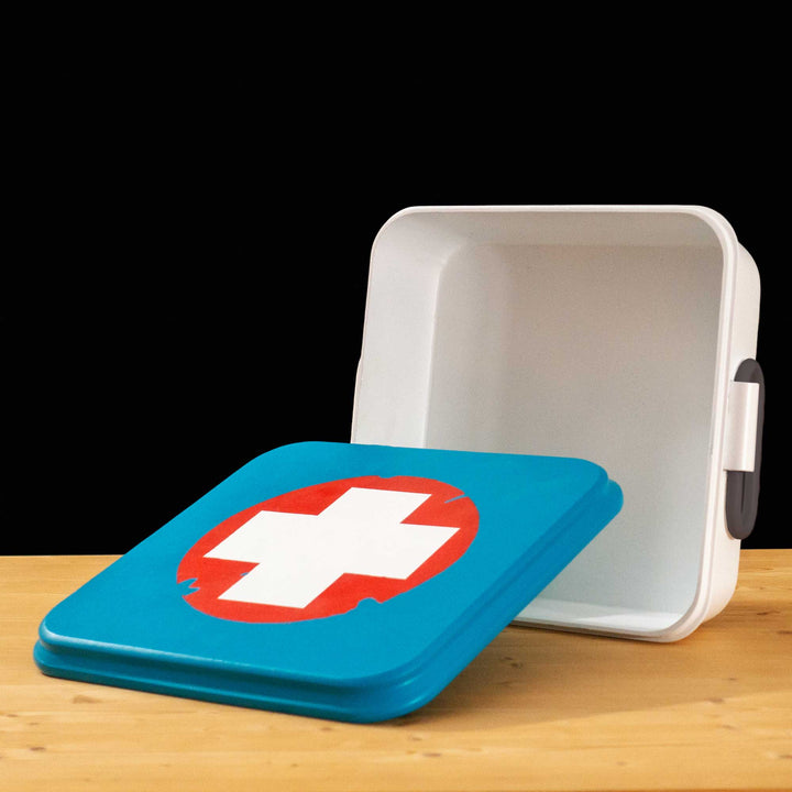 A TF2 Medium Health Kit Replica Props for cosplay featuring its blue lid with a white cross on a chipped paint red circle, the white body and its grey handles.
